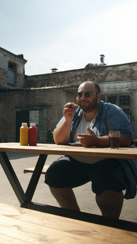 رجل يتناول وجبة سريعة تحتوي على برغر ومشروب غازي في الهواء الطلق، مما يوضح خطر الوجبات السريعة على الصحة.